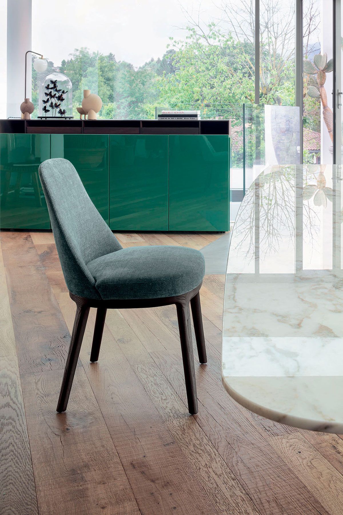 Silla tapizada en verde en una habitación moderna y luminosa con un armario color turquesa y grandes ventanales.