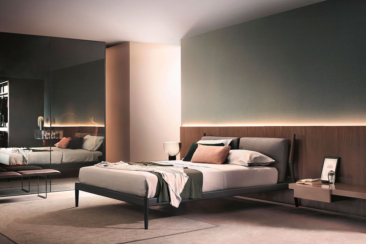 Dormitorio moderno con cama, pared con espejo e iluminación ambiental suave.