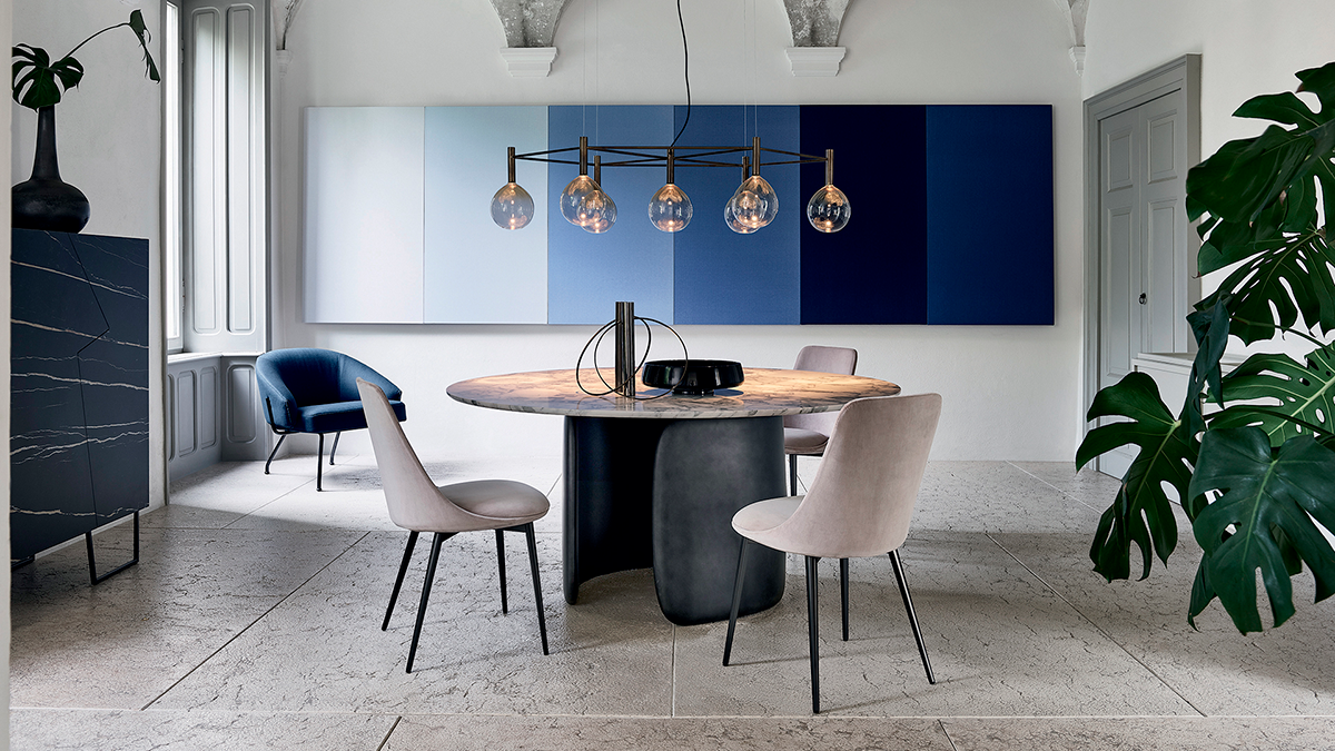 Comedor moderno con mesa redonda, lámparas colgantes, armarios de pared azules y dos sillas.