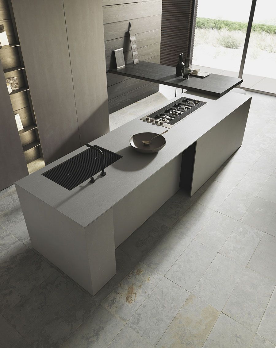 Cocina moderna con isla blanca, placa de cocción integrada, fregadero, lavabo y grandes ventanales.