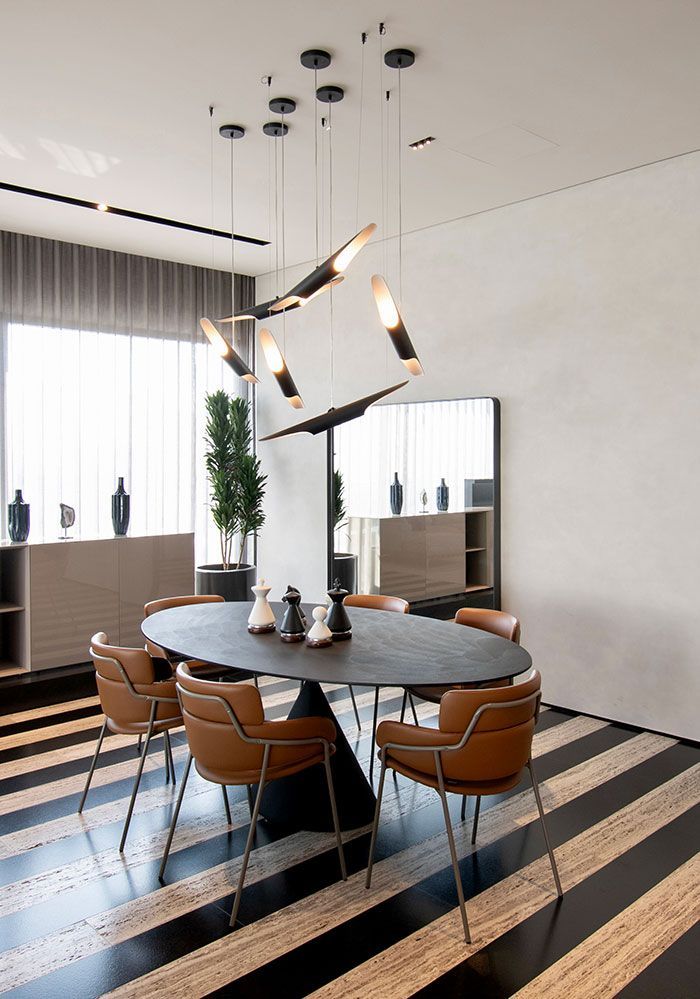Comedor moderno con una mesa larga, sillas color canela, luces negras minimalistas y un sofá gris en primer plano.