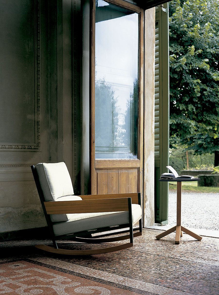 Sillón moderno junto a una ventana abierta en una habitación con alfombra estampada y vistas al jardín.