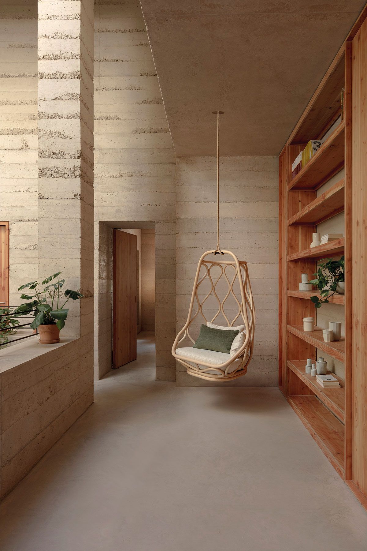 Pasillo minimalista de color beige con una silla colgante de mimbre, estantes empotrados y una planta en maceta.