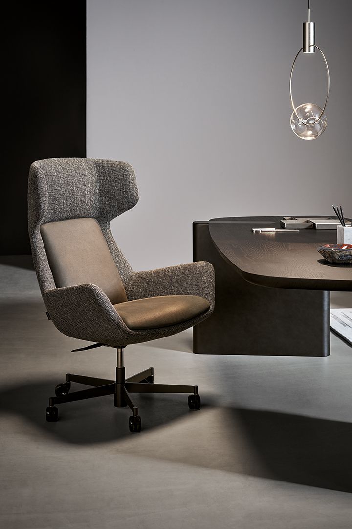 Sillón moderno gris junto a un escritorio oscuro bajo una lámpara colgante en una habitación minimalista.