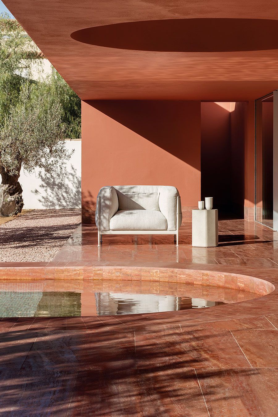 Patio moderno con paredes de terracota, sofá blanco y estanque reflectante bañado por la cálida luz del sol.