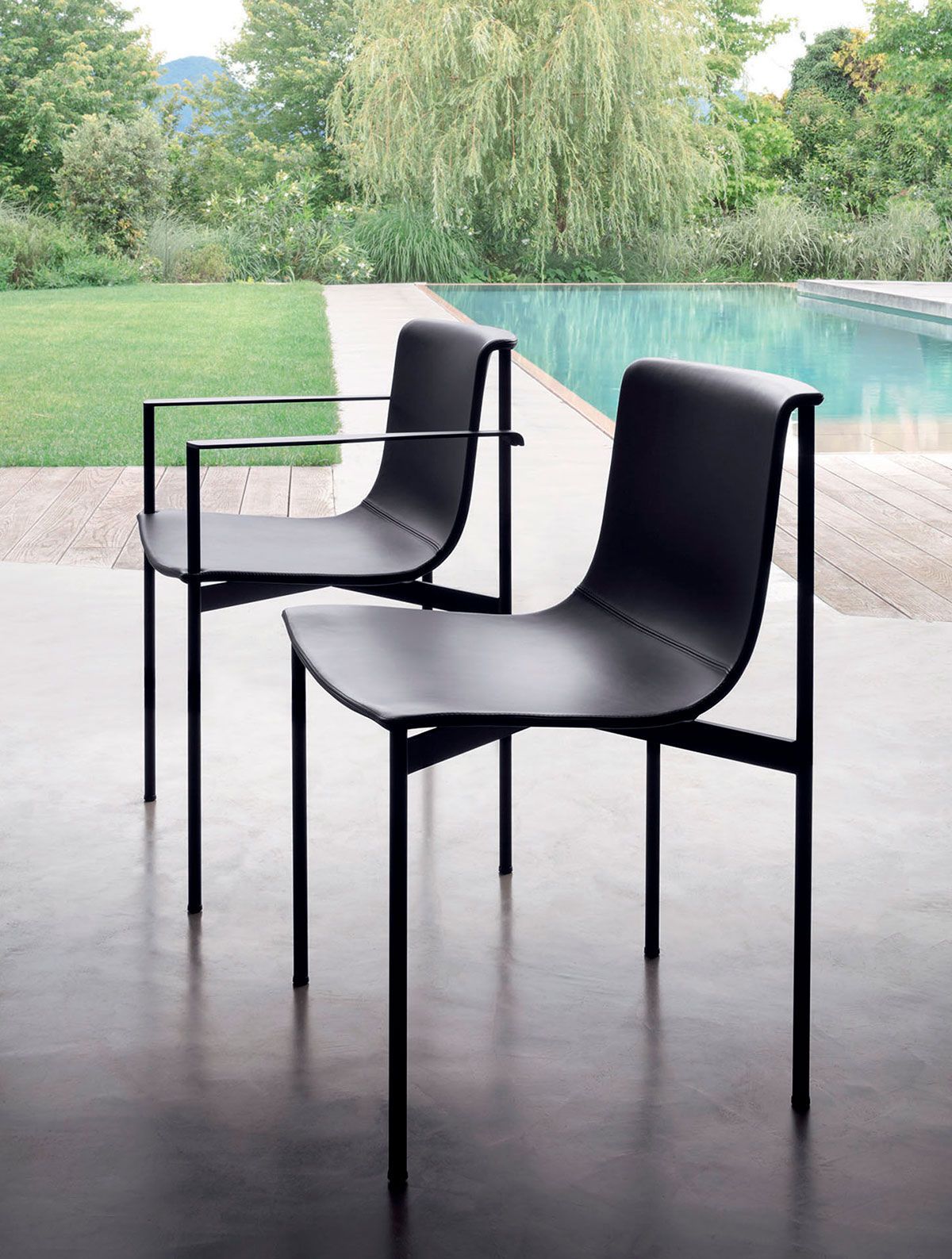 Dos sillas modernas de color negro en un patio junto a una piscina y un jardín.
