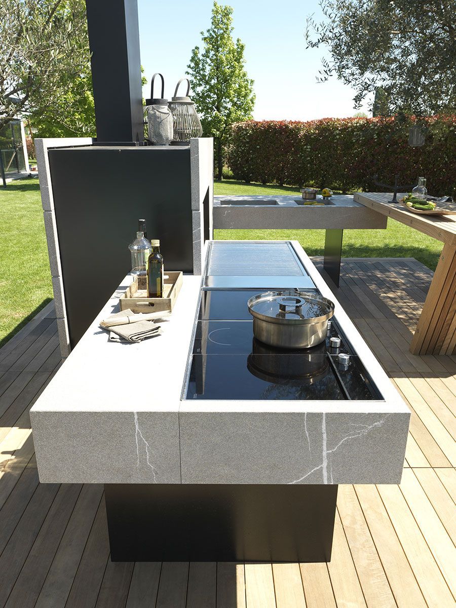 Moderna zona de barbacoa al aire libre con mostrador negro, olla de metal y botella en un patio soleado.
