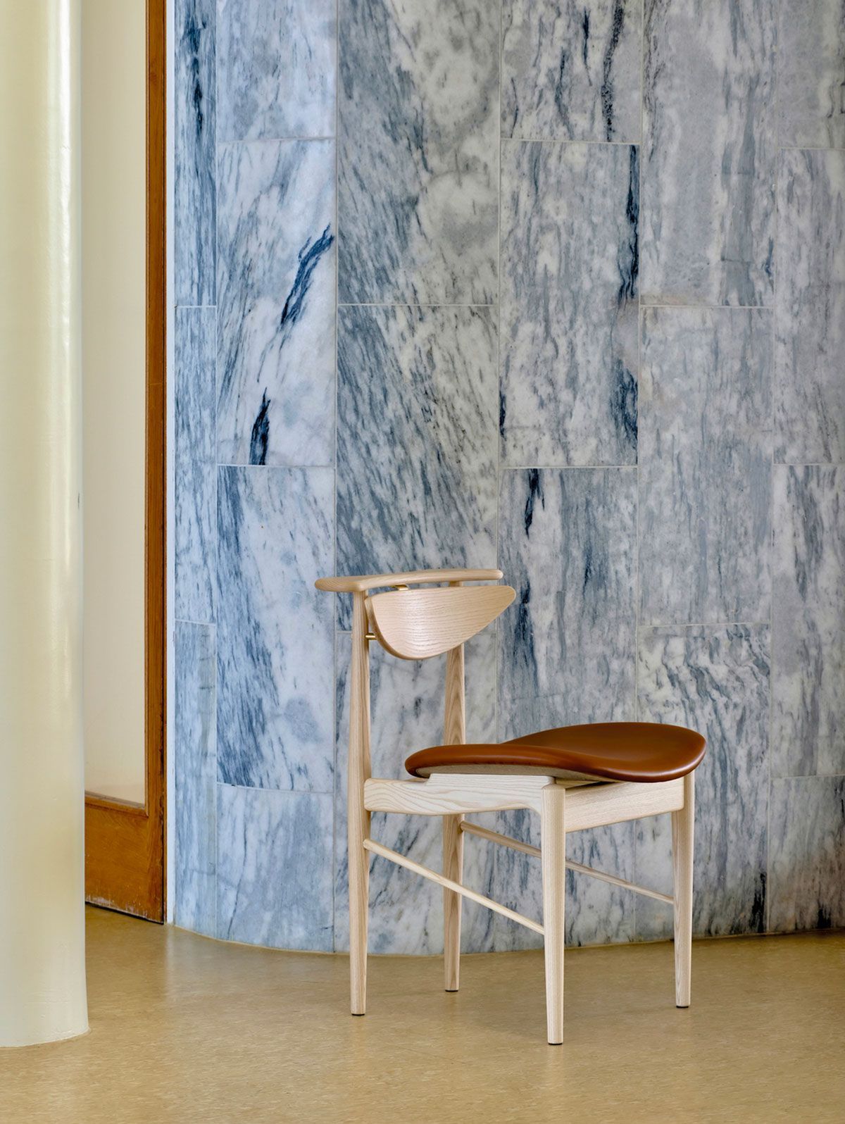 Silla de madera con cojín claro en una habitación con pared con estampado de mármol y cortina color crema.