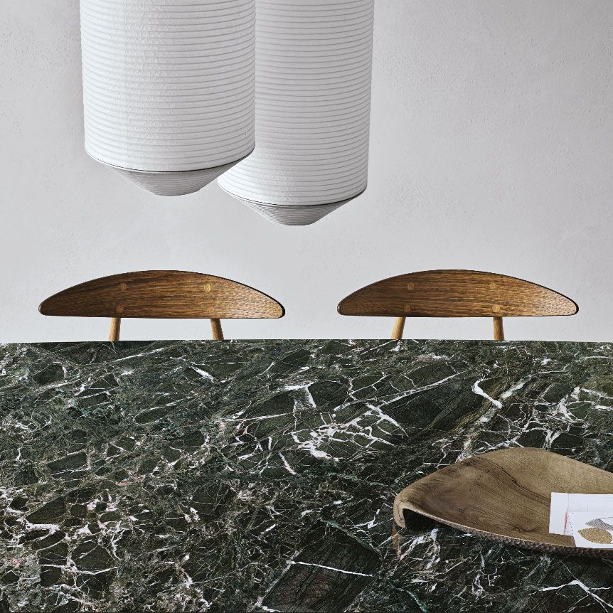 Dos pequeñas sillas de madera detrás de una mesa de mármol verde oscuro, con una tela blanca colgando encima.