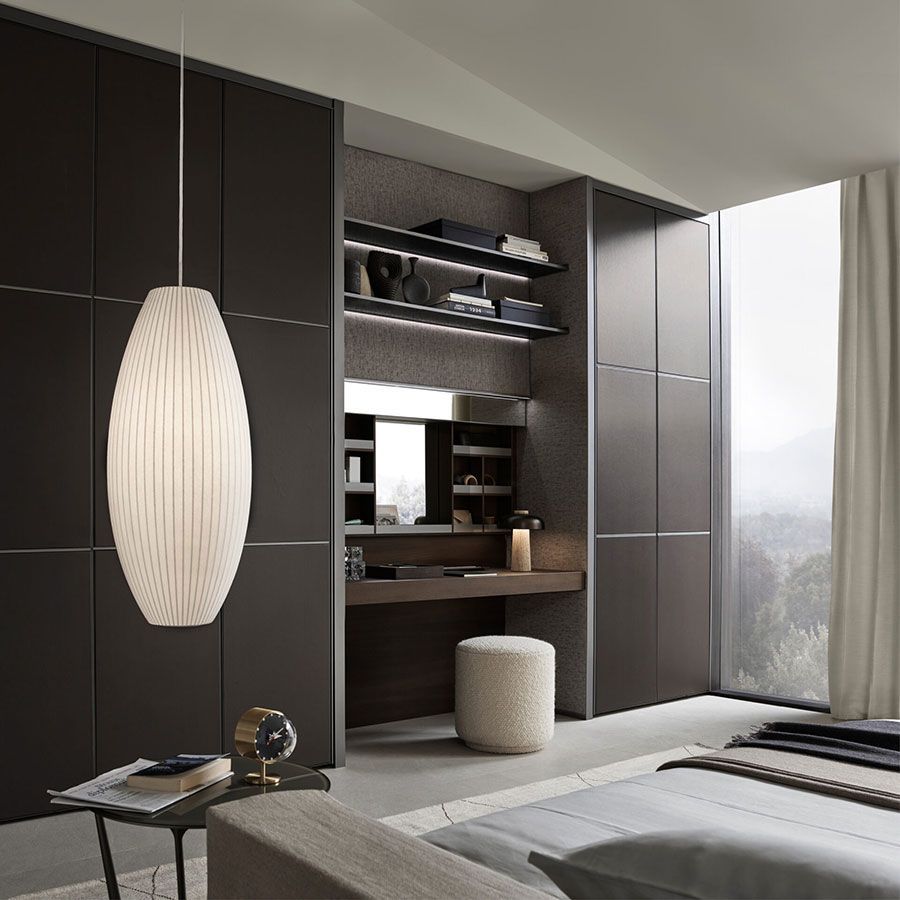 Dormitorio moderno minimalista con armarios empotrados oscuros, rincón de escritorio, lámpara colgante y gran ventanal.
