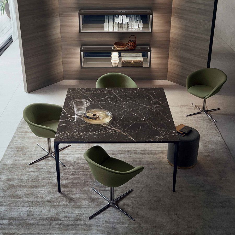 Comedor moderno con mesa de mármol negro, sillas verdes y estanterías empotradas contra paredes revestidas de madera.