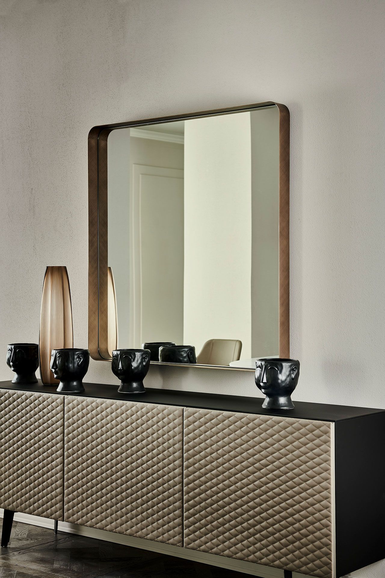 Tocador moderno con un gran espejo, decoración en negro y jarrones de madera en una habitación minimalista.