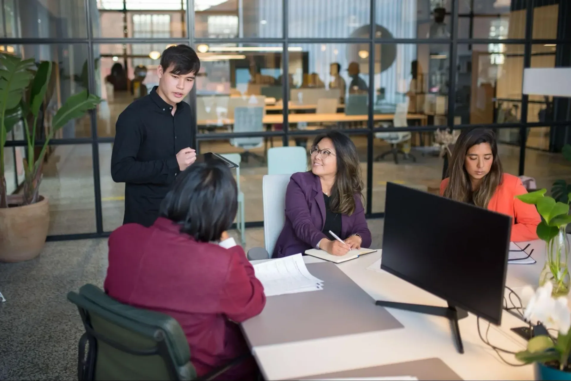 Disengaged employee sitting silently in a team meeting while others actively discuss ideas.