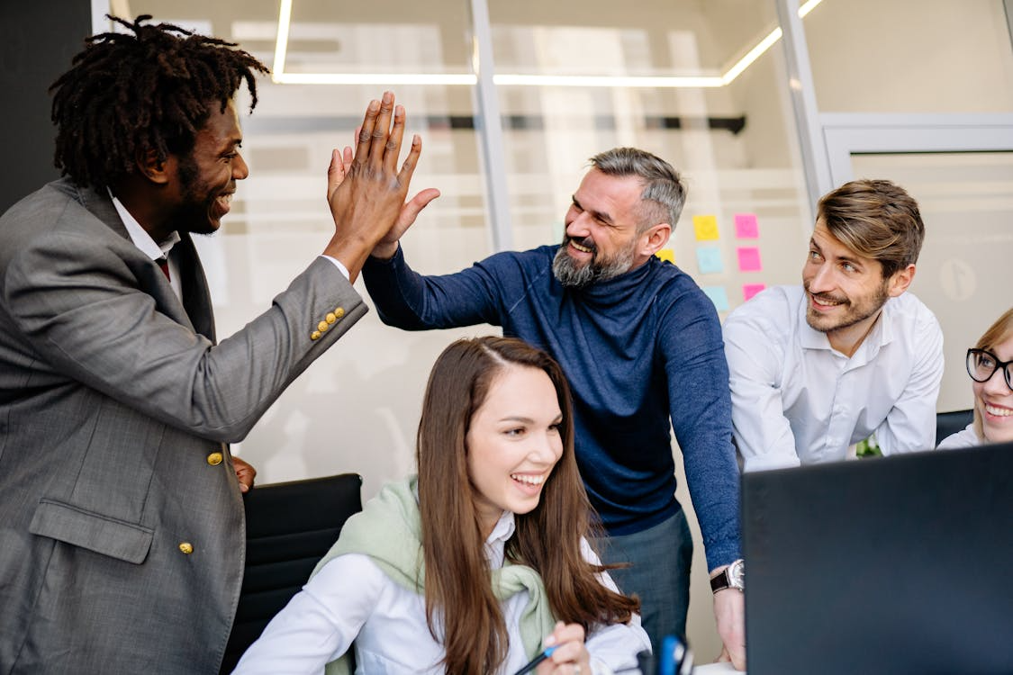 Team celebrating success with high five during meeting, reflecting effective employee engagement solutions.
