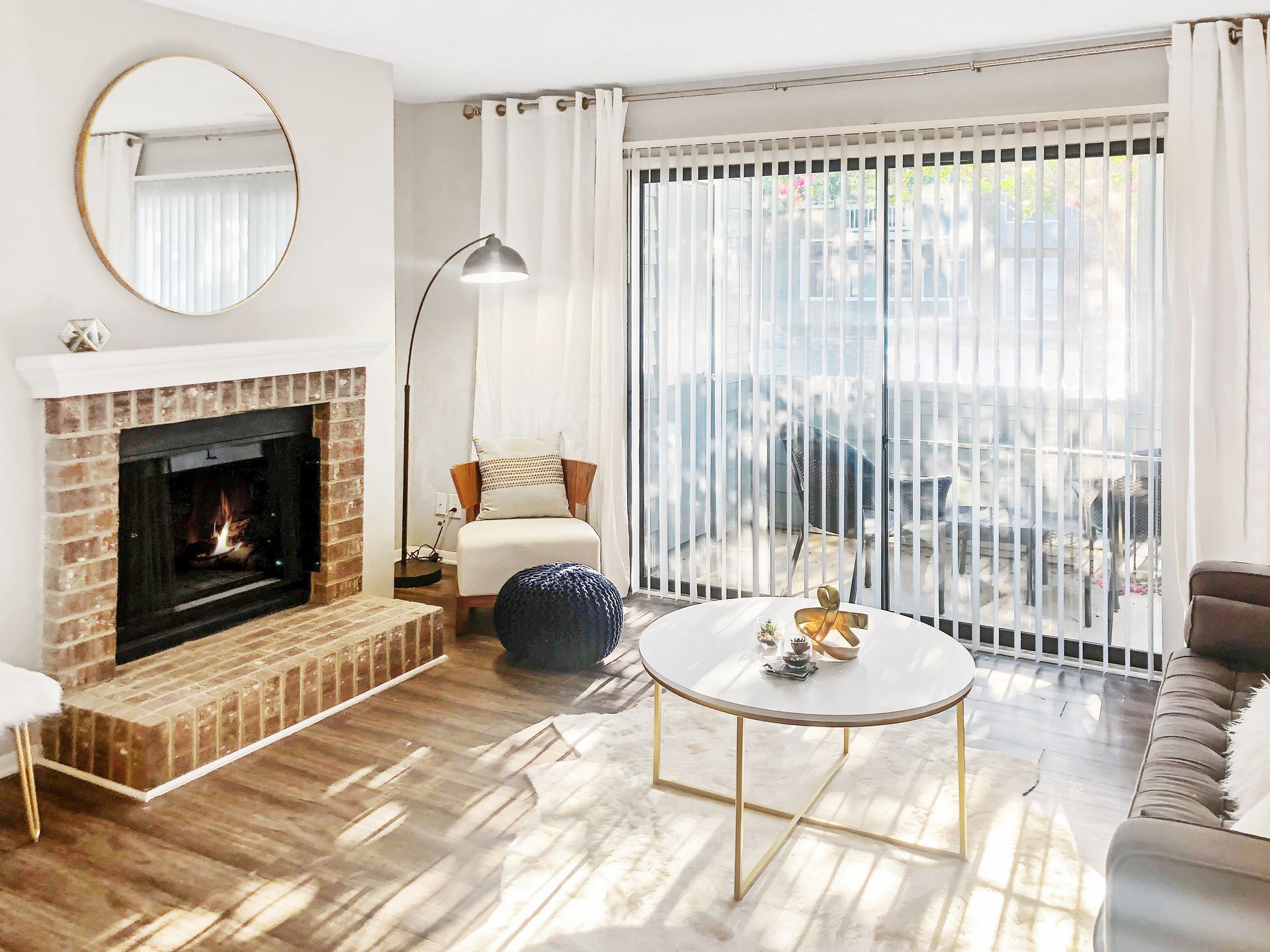 Bright living room with fireplace, large window, sheer curtains, round coffee table, and light sofa at Aurea Station Apartments in South Charlotte, NC.