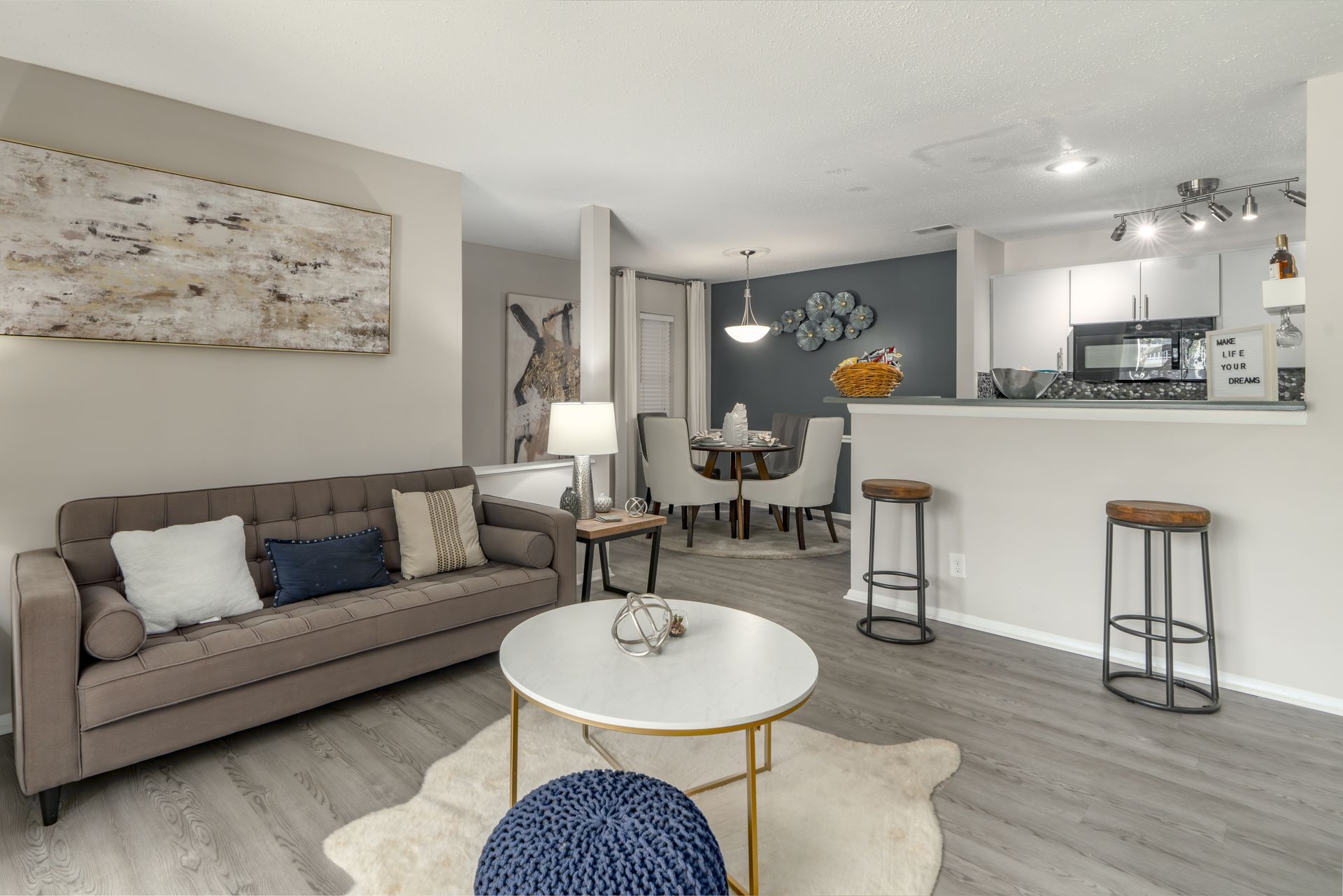 Modern open-concept living room with beige sofa, round coffee table, and kitchen bar stools at Aurea Station Apartments in South Charlotte, NC.