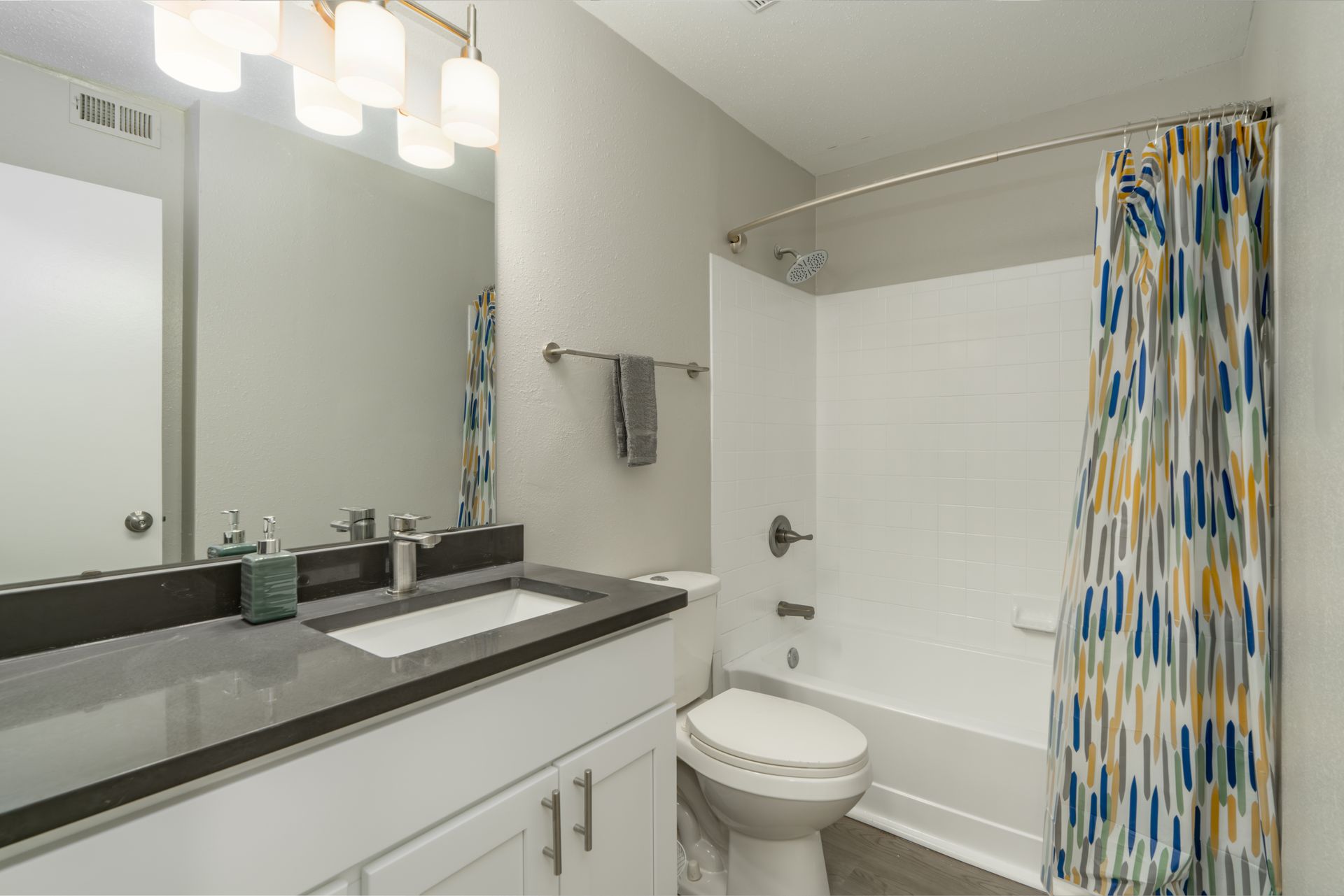 Modern bathroom with white vanity, large mirror, toilet, and patterned shower curtain at Aurea Station Apartments in South Charlotte, NC.