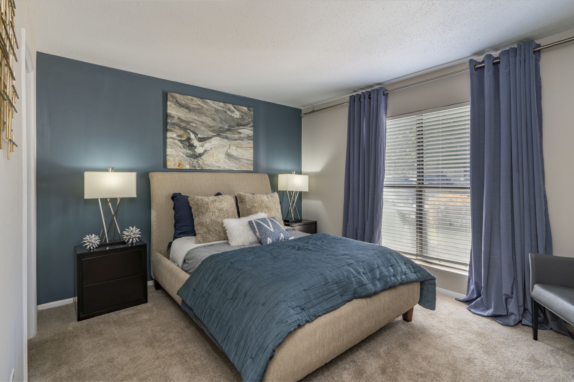 Blue bedroom with a bed, bedside lamps, window blinds, and curtains at Aurea Station Apartments in South Charlotte, NC.