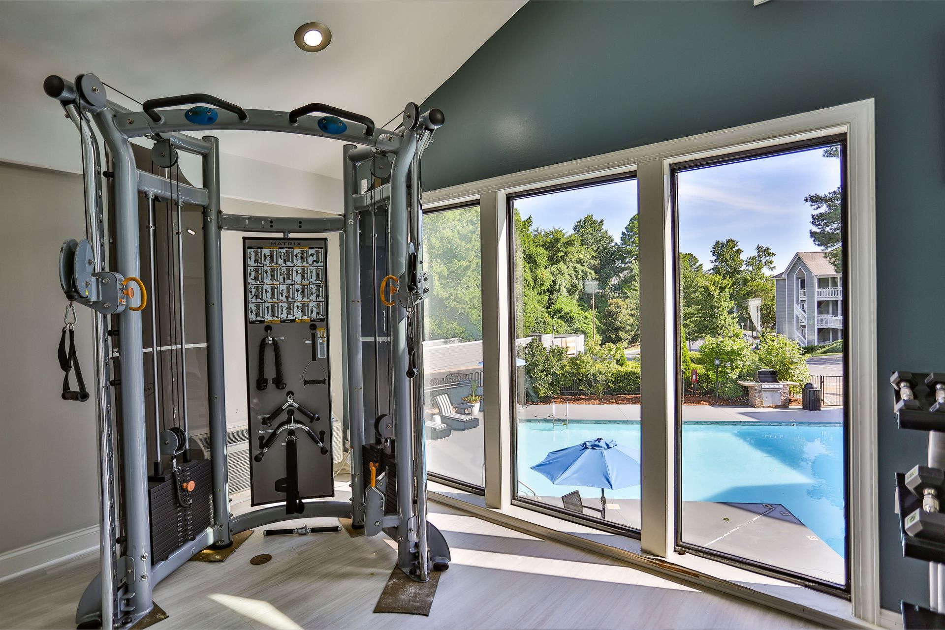 Home gym with cable machine beside sliding glass doors overlooking a backyard pool at Aurea Station Apartments in South Charlotte, NC.