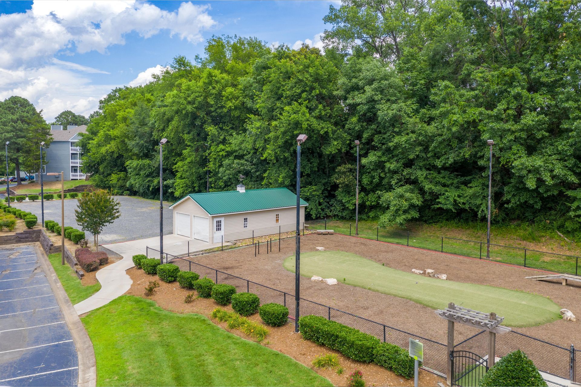 Overhead view of a small fenced sports court beside trees, a parking lot, and a white building at Aurea Station Apartments in South Charlotte, NC.