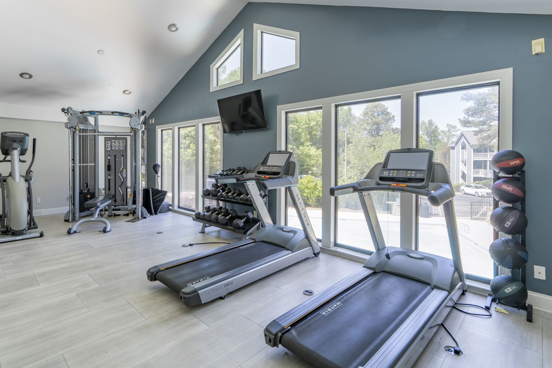 Modern home gym with treadmills, weights, and a cable machine in a bright room at Aurea Station Apartments in South Charlotte, NC.