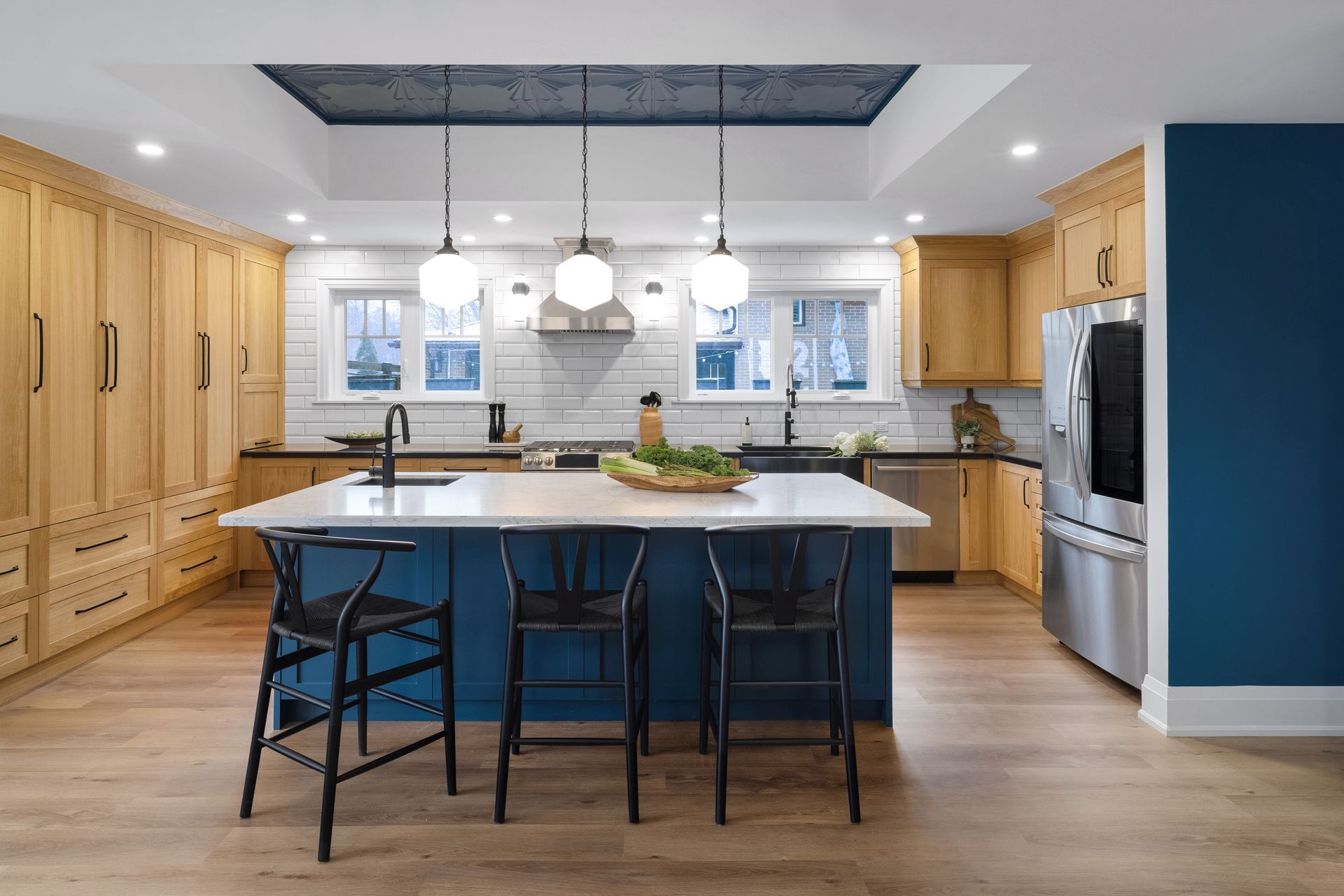 Modern kitchen with light wood cabinets, blue island, pendant lights, and stainless steel appliances