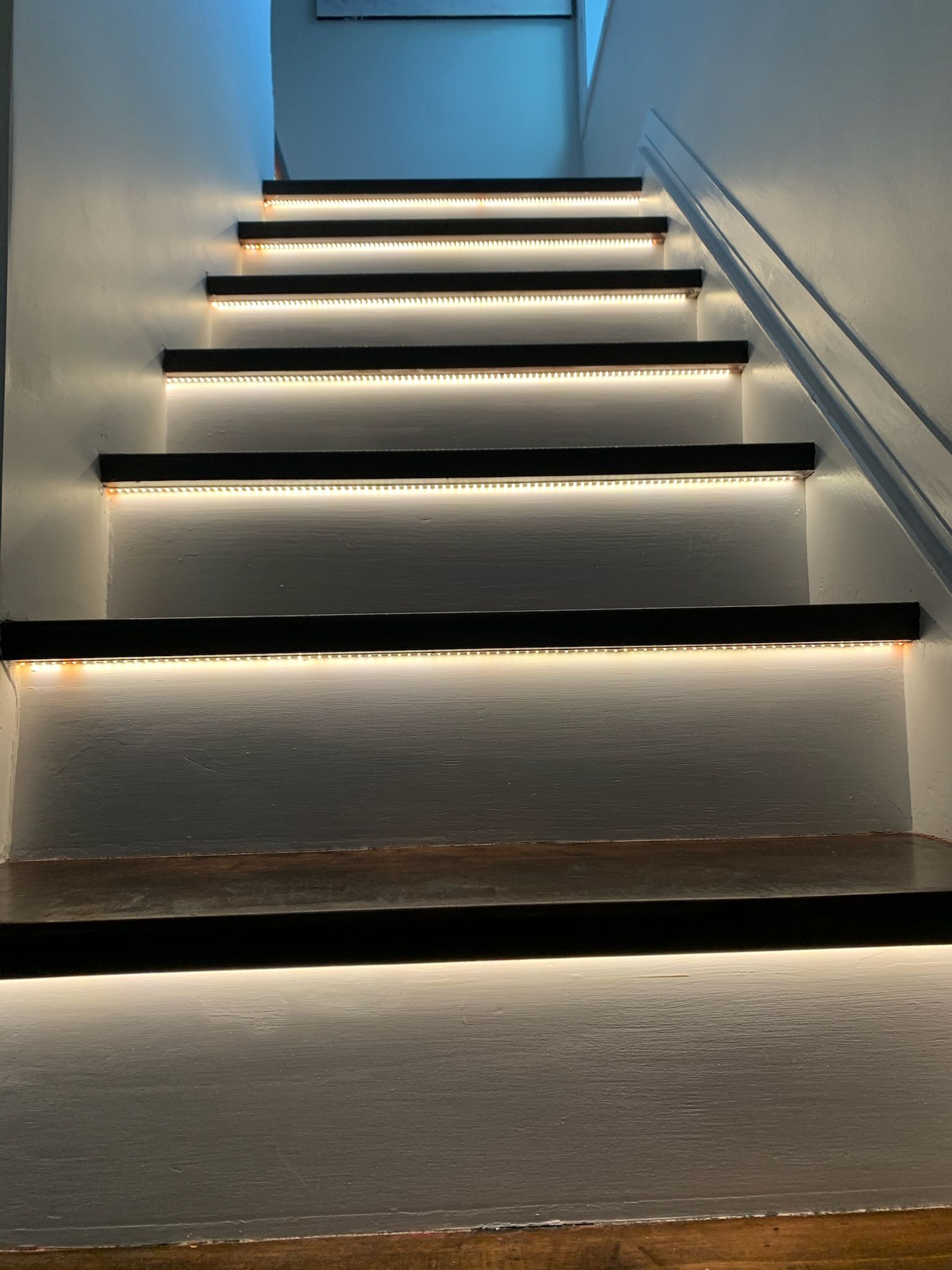 Dim staircase with LED strip lighting along each step in a narrow indoor hallway