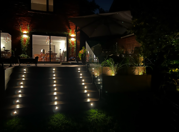 Nighttime entrance with illuminated steps leading to a warmly lit modern home and garden lights