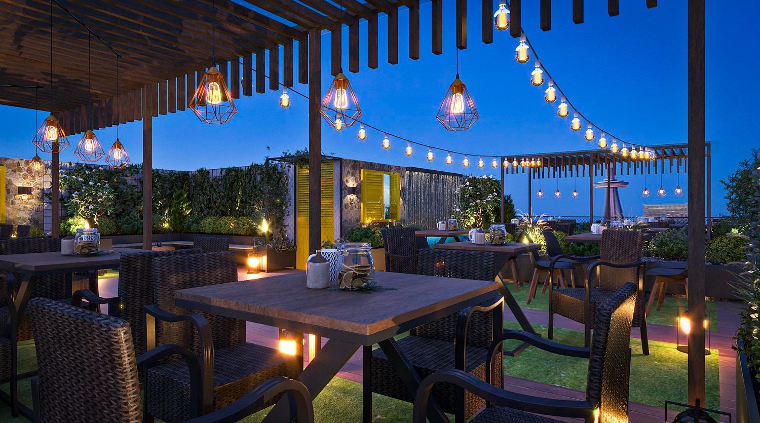 Outdoor patio dining area at dusk with string lights, wooden tables, and chairs overlooking a city view