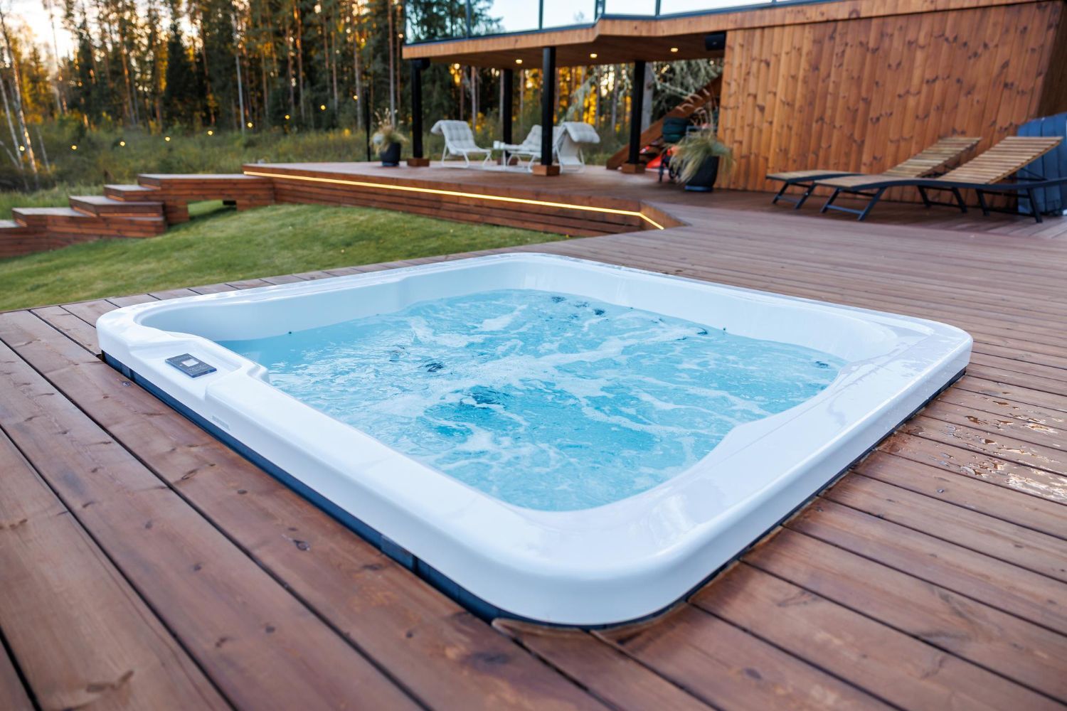 White above-ground hot tub bubbling on a wooden deck beside a house and lawn
