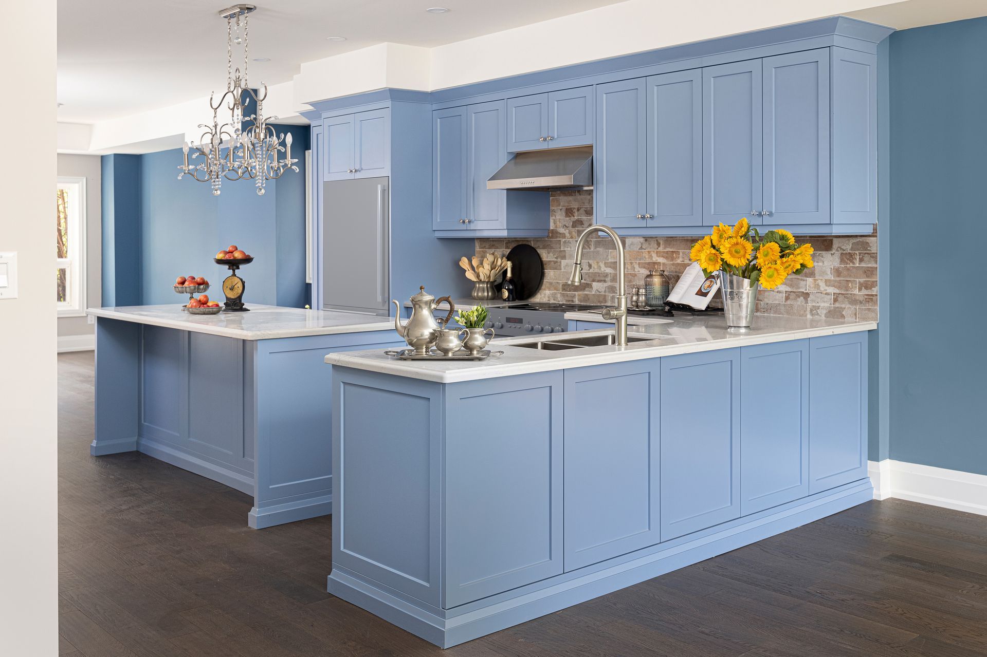 Light blue kitchen with white island, marble counters, chandelier, and yellow flowers