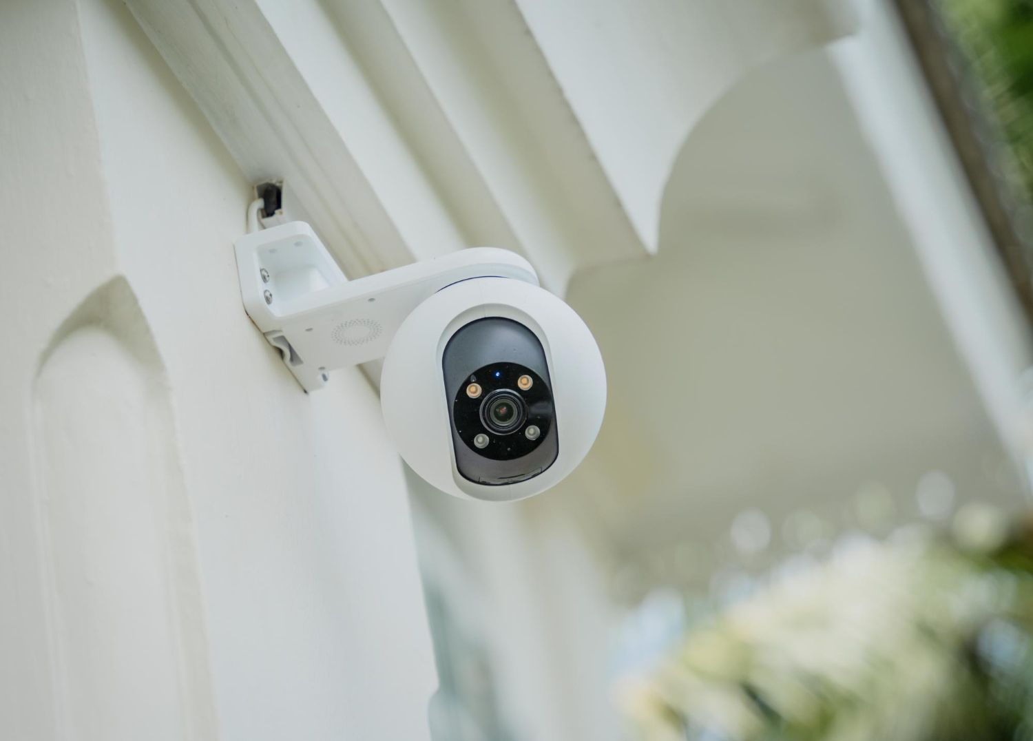 A white, spherical outdoor security camera mounted on a white exterior wall.