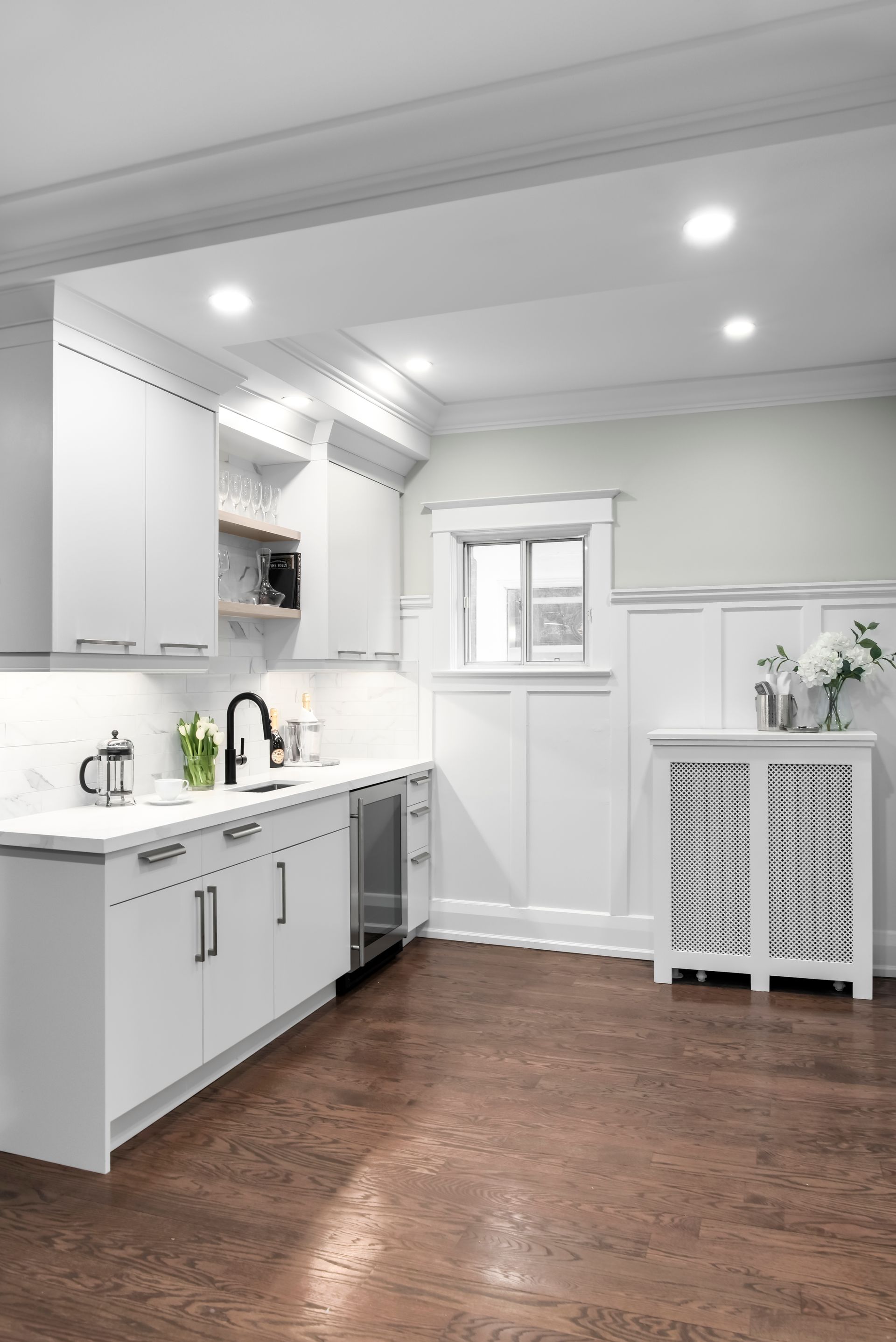 Modern white kitchen with stainless steel appliances, dark faucet, and a copper-colored floor.