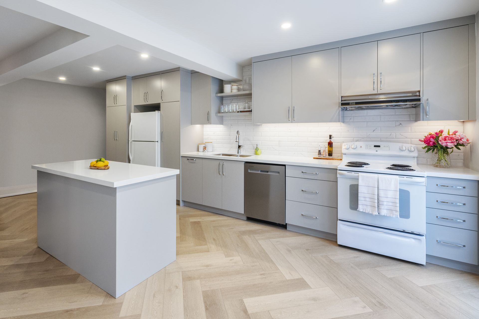 Modern kitchen with light gray cabinets, white appliances, and wooden floor.