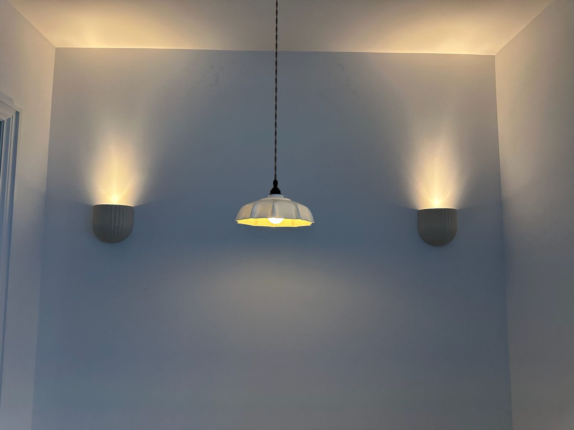 White wall with pendant light centered between two sconces, all lit.