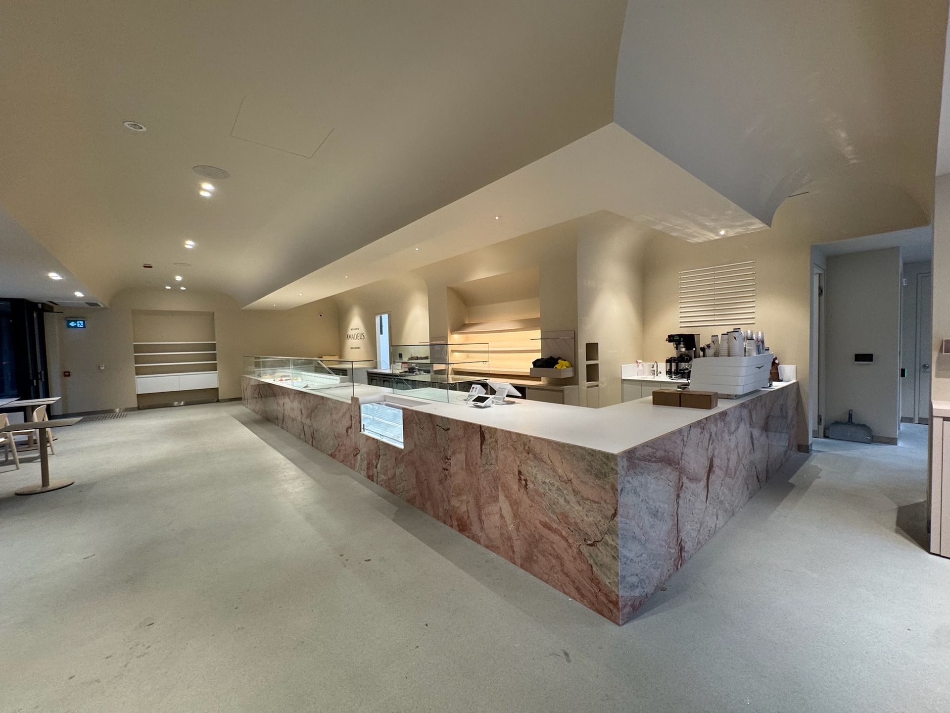 Interior view of a cafe with a pink marble counter, white ceiling, and various displays; ready for opening.