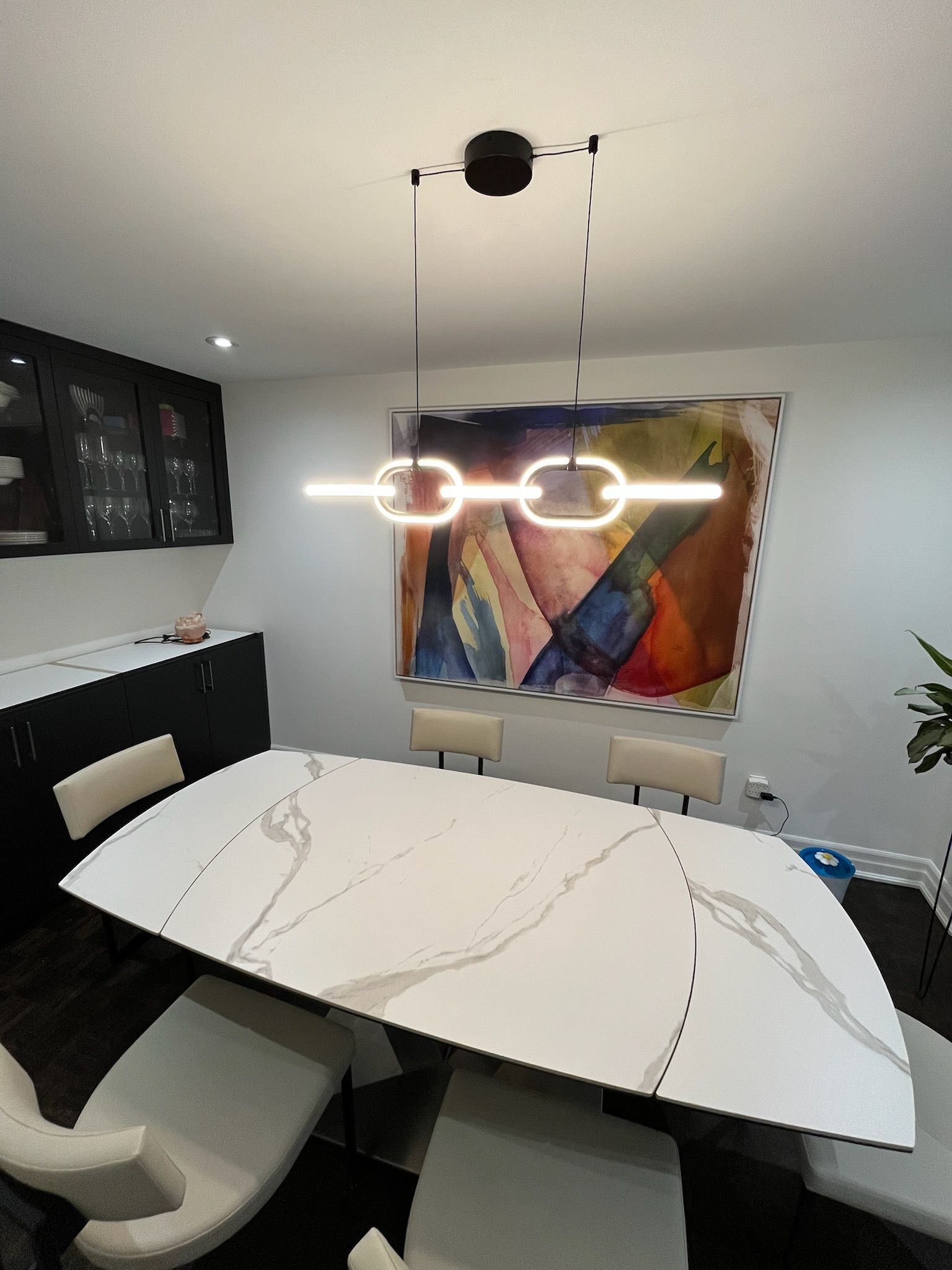 Dining room with white marble table, modern light fixture, and colorful artwork.