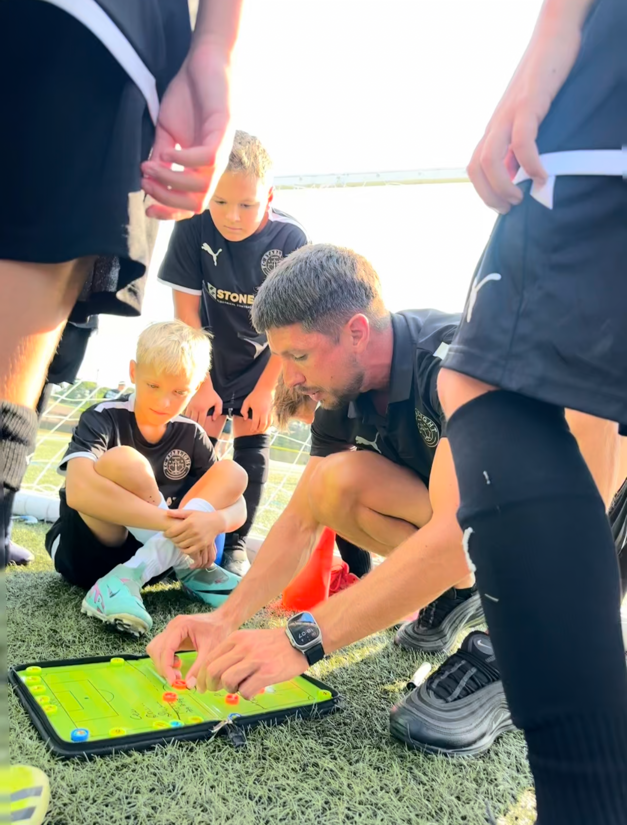 Soccer coach pointing to plays on a tactics board with players, on a field.