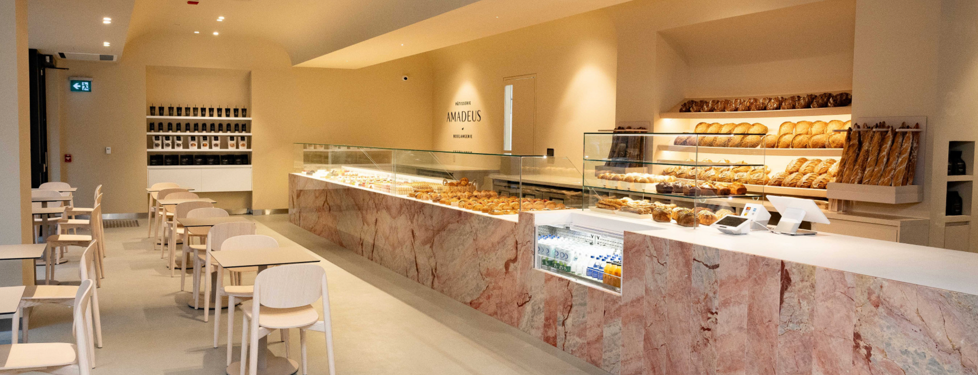 Interior of a bakery with tables and a display counter full of pastries.