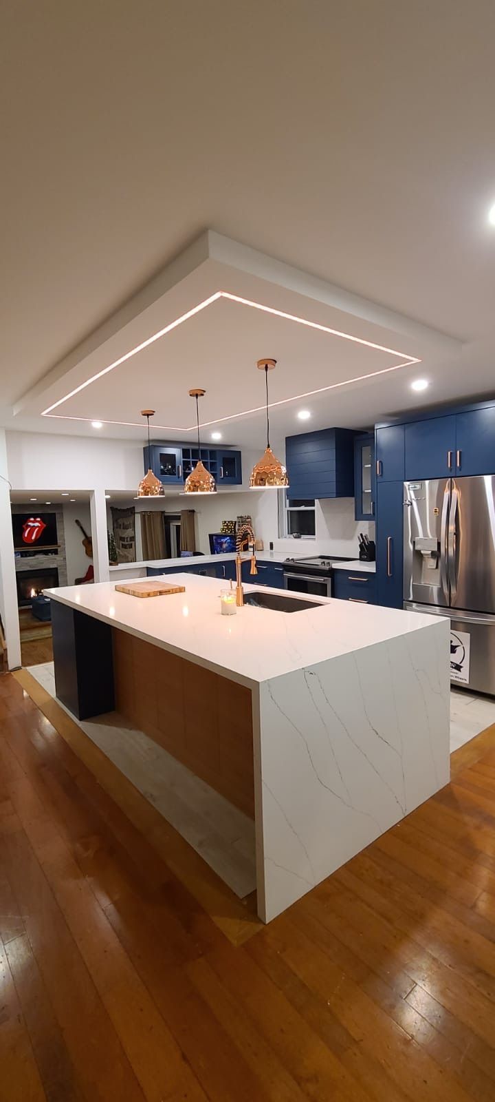 Modern kitchen with large island, navy cabinets, and wood floors. Recessed lighting in ceiling.