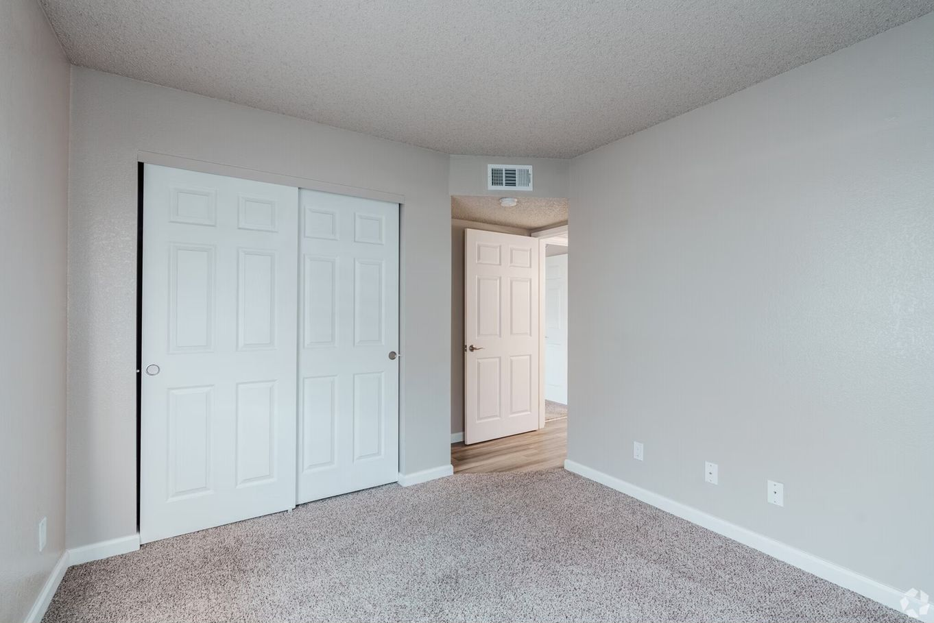 Empty bedroom with gray walls, white closet doors, and beige carpet.