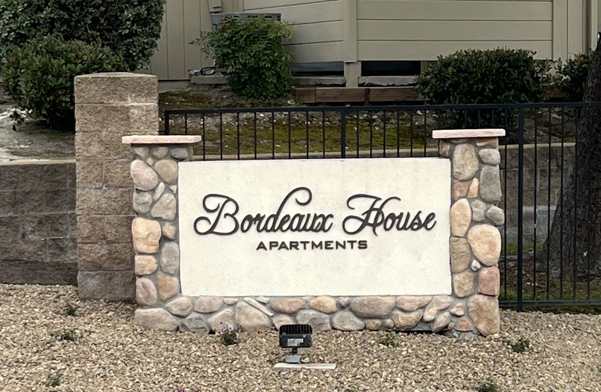 Bordeaux House Apartments sign with stone accents and black wrought iron fence.