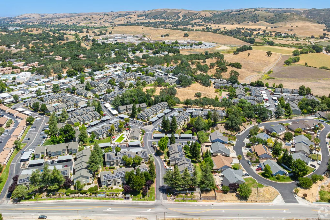 Aerial view of a residential community with houses and roads, surrounded by dry, hilly terrain.