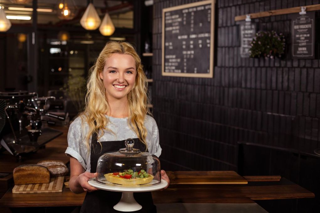 Smiling chef holding a decorated cake in a cozy café with hanging lights and menu boards
