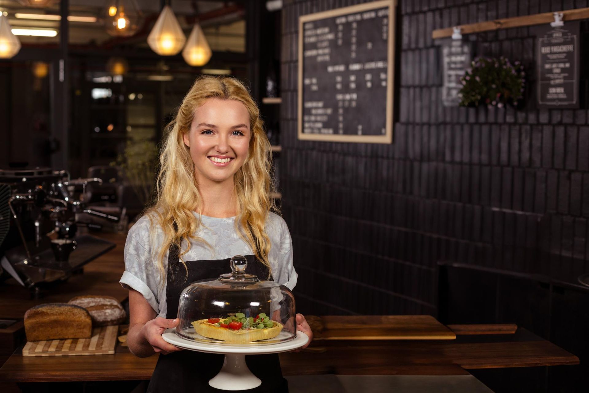 Smiling chef holding a decorated cake in a cozy café with hanging lights and menu boards