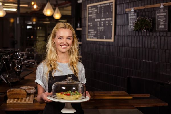 Smiling chef holding a decorated cake in a cozy café with hanging lights and menu boards