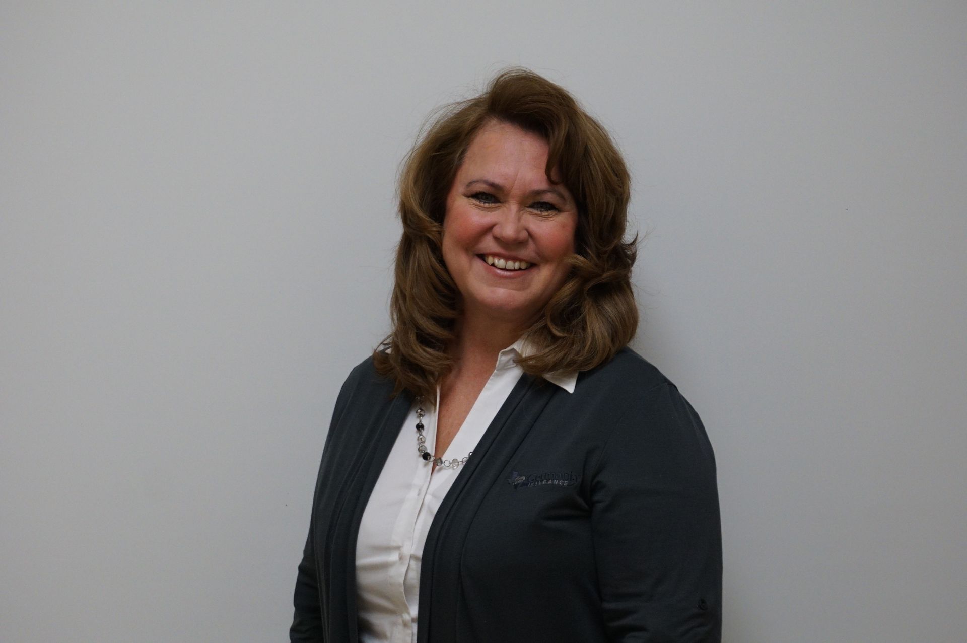 Smiling woman in a dark blazer and white blouse against a plain light gray background