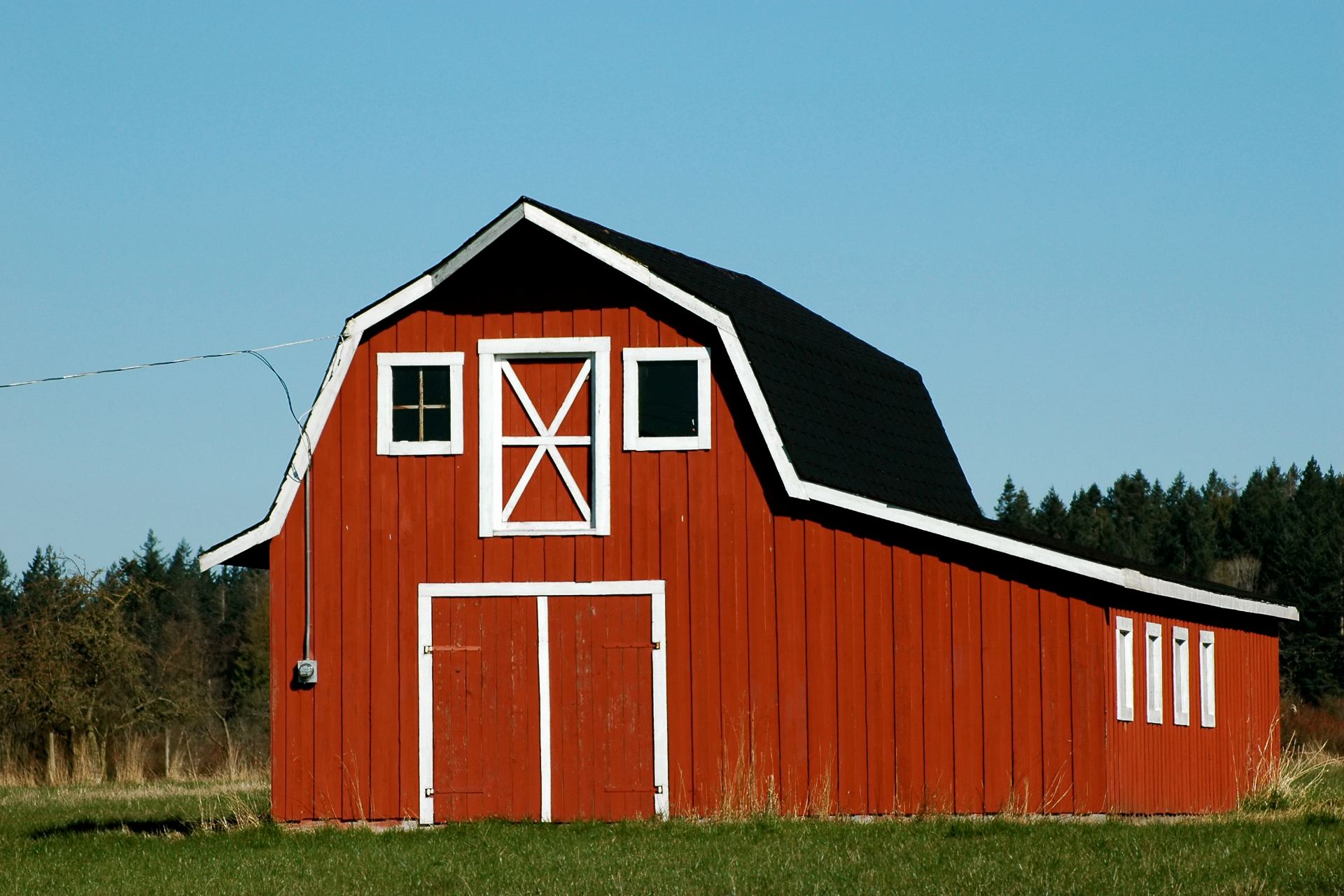 Red barn with white trim and black roof in a grassy field under a blue sky