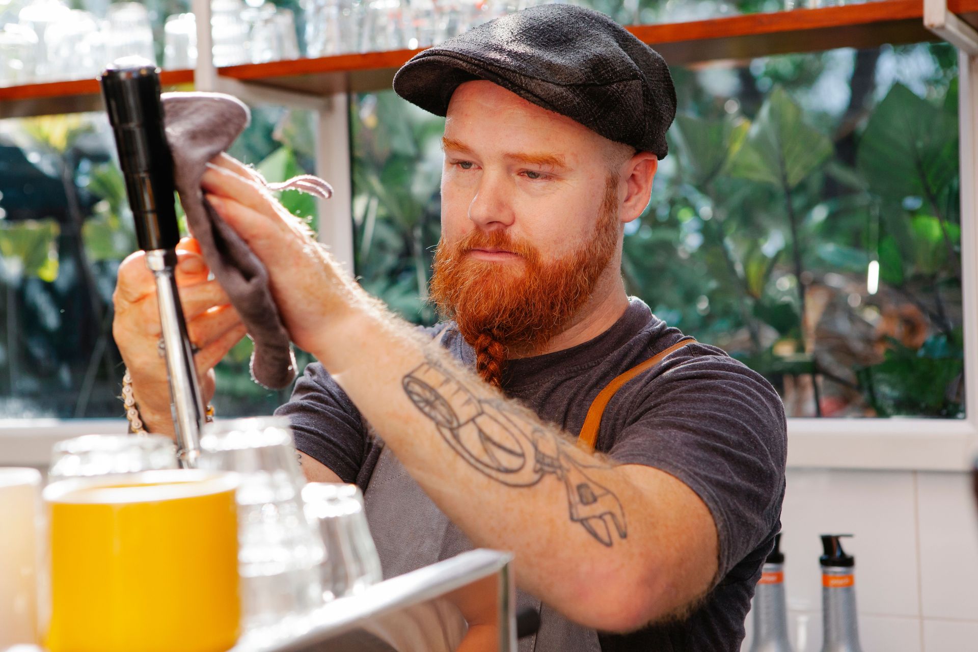 Bartender pulling a beer tap in a bright bar, with a glass of golden beer in the foreground.