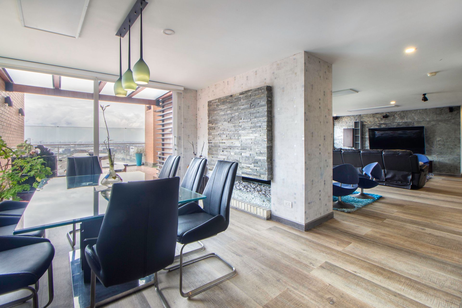 Modern open-plan apartment with dining table, black chairs, lounge area, and large windows overlooking a balcony